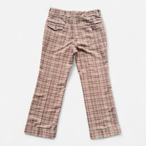 May include: Brown plaid pants with a wide leg and two back pockets. The pants have a button closure and belt loops. The plaid pattern is a mix of brown and cream colors. The pants are made of a woven fabric.