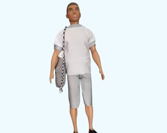 May include: A plastic doll with a short haircut wearing a white short-sleeved shirt with grey trim, matching grey knee-length shorts, and black sandals. The doll carries a grey textured shoulder bag with a black and white braided strap.