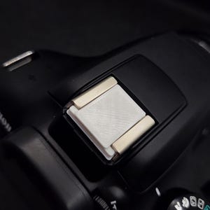 Könnte beinhalten: Eine schwarze Kamera mit einem weißen Blitzdiffusor, der oben angebracht ist. Die Kamera hat ein Moduswahlrad mit verschiedenen Einstellungen.