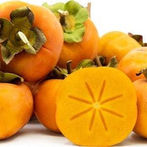 May include: A collection of ripe persimmons, with a vibrant orange hue and green leafy tops. One persimmon is sliced open, revealing a star-shaped pattern in the flesh. The fruits are arranged on a white surface.