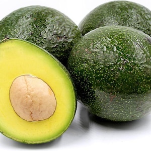 May include: Four ripe avocados, one cut in half to reveal the creamy yellow flesh and large seed. The avocados have a dark green, textured skin. The cut avocado shows a vibrant yellow interior.