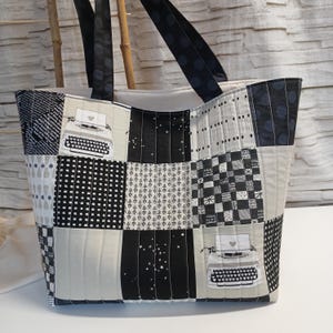 Könnte beinhalten: Eine Patchwork-Tragetasche in Schwarz, Weiß und Grau. Die Tasche weist eine Vielzahl von Mustern auf, darunter Quadrate, Punkte und ein Schreibmaschinendesign. Die Griffe sind schwarz mit weißen Tupfen. Die Tasche ist aus gestepptem Stoff gefertigt.