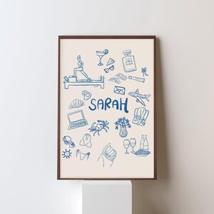 Op de afbeelding: Een blauwe en witte geïllustreerde print met de naam "SARAH" in het midden. De print bevat verschillende afbeeldingen, waaronder een croissant, een laptop, een krab, een boeket bloemen, een glas wijn, een vliegtuig, een fles parfum, een zonnebril, een martini-glas, een stuk pizza, oorbellen, lippenstift, een schelp, een badpak en een zon.