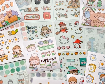 以下が含まれることがあります： かわいい漫画のキャラクター、食べ物、その他の幻想的なデザインが施されたカラフルなステッカーのコレクション。ステッカーは薄い青色の背景に配置されています。一部のステッカーには日本語が書かれており、「マジック」、「バターフライ」、「寿司を食べる！」などがあります。