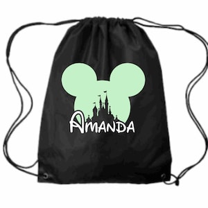 May include: Black drawstring bag with a white Mickey Mouse head silhouette and a white silhouette of Cinderella's castle. The text "Amanda" is printed below the castle.