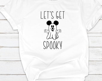 Może przedstawiać: Biały t-shirt z krótkim rękawem z czarną grafiką ducha z mysimi uszami oraz napisem "LET'S GET SPOOKY" wydrukowanym prostą czcionką bezszeryfową. Koszulka ma okrągły dekolt i jest zawiązana w supeł u dołu z przodu.
