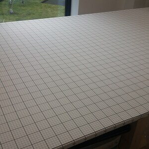 以下が含まれることがあります： グリッドパターンを持つ、長方形の大きなカッティングマット。 マットは薄いグレーで、黒いグリッド線があり、正確な測定とカットのための視覚的なガイドを提供します。 マットは木製の表面に置かれています。