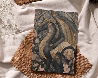 May include: A decorative journal featuring a detailed illustration of a dragon with black and gold wings, set against a backdrop of floral elements. The dragon is the focal point, with intricate scales and a majestic pose. The color palette includes shades of black, gold, and muted greens.