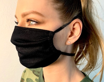 May include: A black face mask with pleats, worn by a person with long brown hair pulled back in a ponytail. The mask has elastic ear loops.