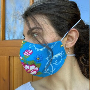 May include: A person wearing a blue face mask with a floral pattern. The mask has white and pink flowers on a blue background.