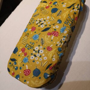 May include: A yellow fabric cover with a floral pattern featuring blue flowers, red and white mushrooms, and green leaves.