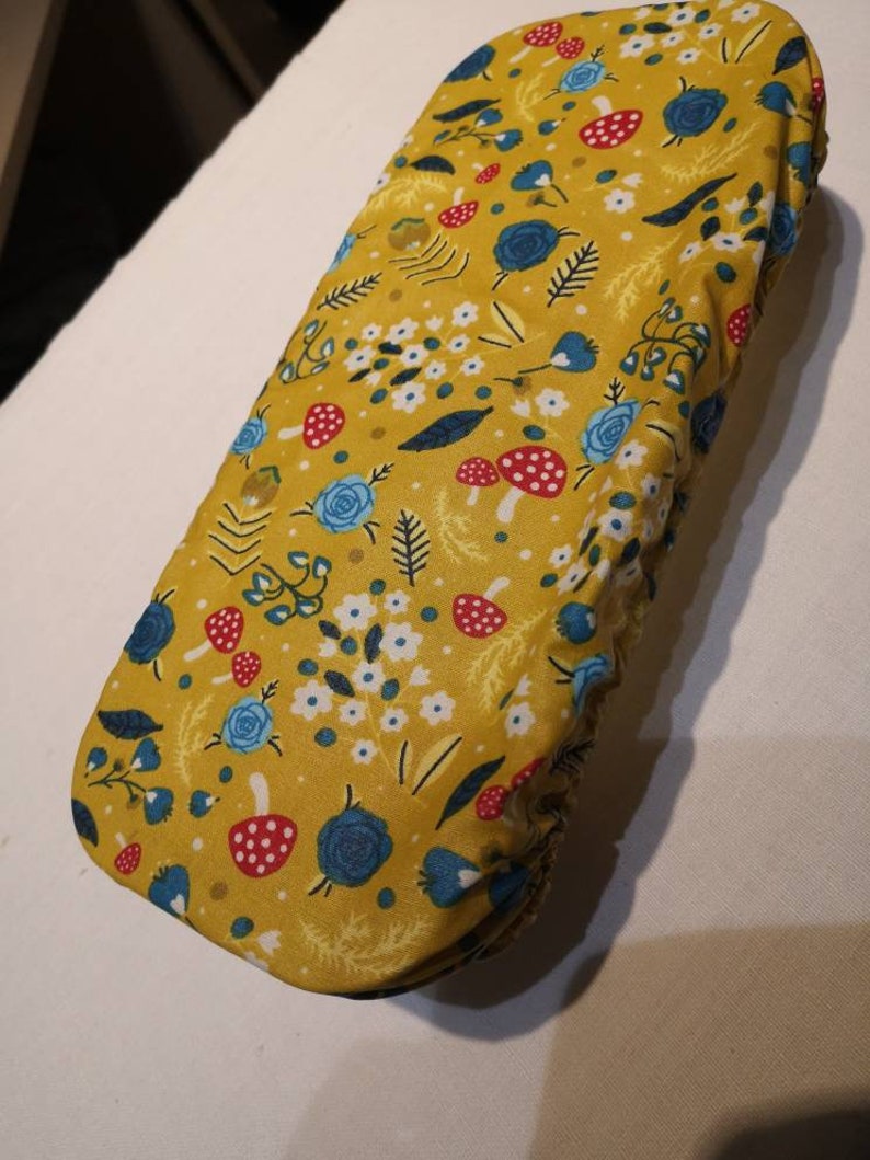 May include: A yellow fabric cover with a floral pattern featuring blue flowers, red and white mushrooms, and green leaves.