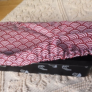 Peut inclure: Un couvre-pain en tissu rouge et blanc à motif. Le couvre-pain est fait d'un tissu doux et extensible et a un bord festonné. Le couvre-pain est posé sur un moule à pain noir.