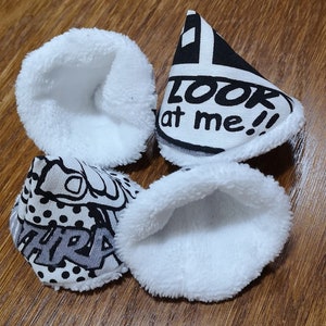 Puede incluir: Cuatro conos de tela blanca con diseños de estilo cómic en blanco y negro. Los diseños incluyen las palabras "¡Mírame!" y "¡Bang!"