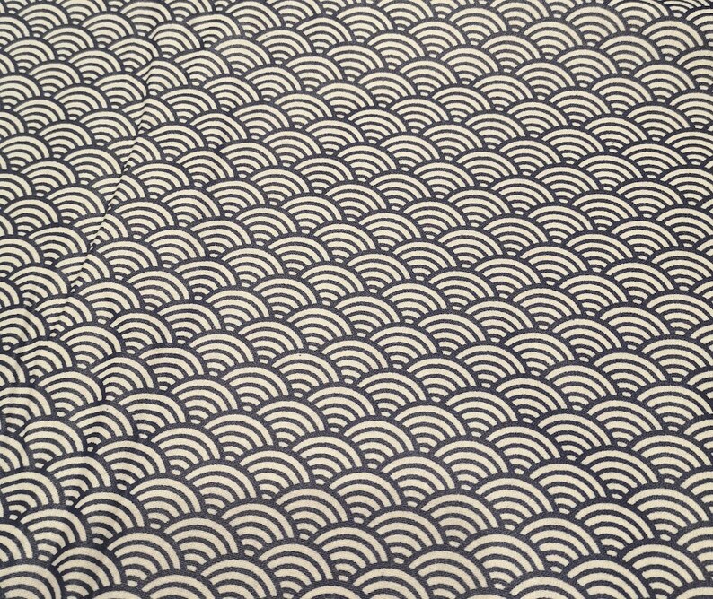 May include: A close-up of a fabric with a repeating pattern of black and white overlapping semi-circles. The pattern resembles scales or waves.