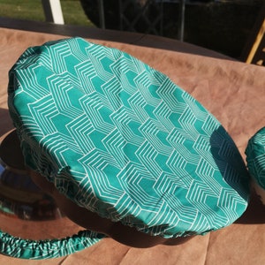 K&ouml;nnte beinhalten: Ein Sch&uuml;sseldeckel aus Stoff mit einem Muster in Teal und Wei&szlig;. Der Deckel hat ein geometrisches Design mit wei&szlig;en Linien auf einem Teal-Hintergrund.
