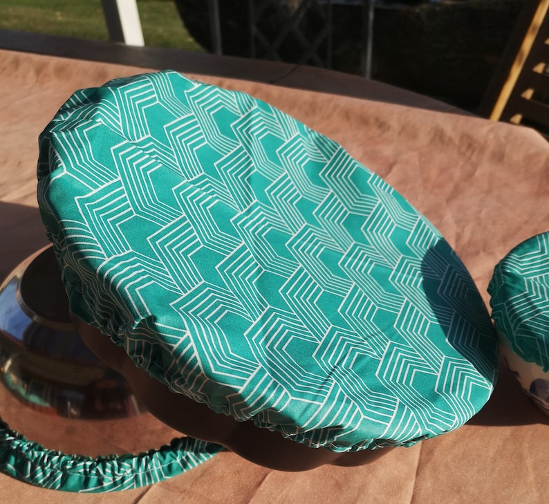 K&ouml;nnte beinhalten: Ein Sch&uuml;sseldeckel aus Stoff mit einem Muster in Teal und Wei&szlig;. Der Deckel hat ein geometrisches Design mit wei&szlig;en Linien auf einem Teal-Hintergrund.