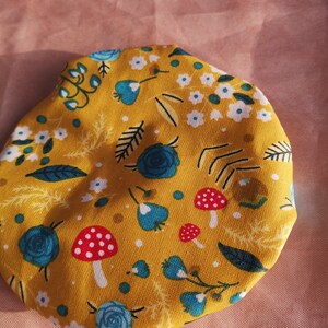 K&ouml;nnte beinhalten: Ein gelber Stoffkreis mit einem Blumenmuster mit blauen Blumen, wei&szlig;en Blumen, gr&uuml;nen Bl&auml;ttern und roten und wei&szlig;en Pilzen.