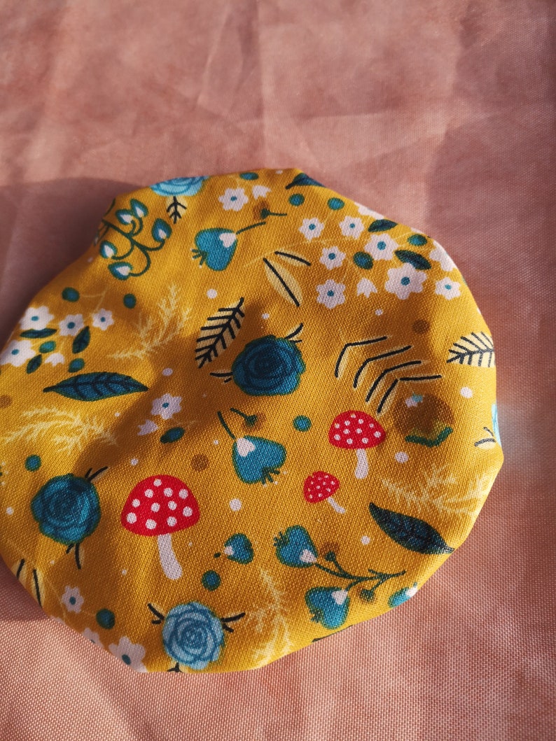 K&ouml;nnte beinhalten: Ein gelber Stoffkreis mit einem Blumenmuster mit blauen Blumen, wei&szlig;en Blumen, gr&uuml;nen Bl&auml;ttern und roten und wei&szlig;en Pilzen.