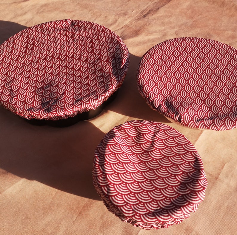 K&ouml;nnte beinhalten: Drei wiederverwendbare Lebensmittel-Abdeckungen in verschiedenen Gr&ouml;&szlig;en mit einem roten und wei&szlig;en Muster. Die Abdeckungen sind aus Stoff und haben ein gewelltes Design.