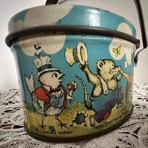 Puede incluir: Una fiambrera vintage de metal azul y blanco con asa. La fiambrera presenta una ilustraci&oacute;n caprichosa de un p&aacute;jaro, un oso y una mariposa. El texto "UNC' BILLY POSS INC" y "WALDO WREN" est&aacute; impreso en la fiambrera.
