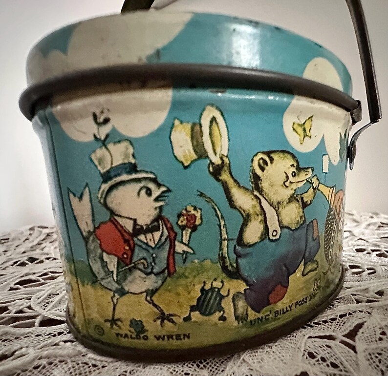 Puede incluir: Una fiambrera vintage de metal azul y blanco con asa. La fiambrera presenta una ilustraci&oacute;n caprichosa de un p&aacute;jaro, un oso y una mariposa. El texto "UNC' BILLY POSS INC" y "WALDO WREN" est&aacute; impreso en la fiambrera.