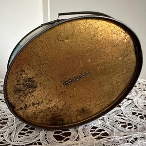 Puede incluir: Una lata de metal vintage con interior dorado y asa negra. La lata tiene una etiqueta que dice "Golden Nut."