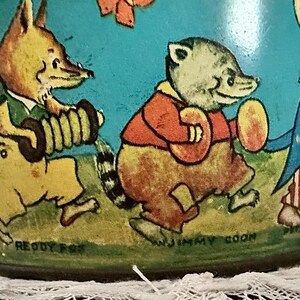 Puede incluir: Una fiambrera vintage de metal con una ilustraci&oacute;n colorida de cuatro animales de dibujos animados tocando m&uacute;sica. Los animales son un zorro tocando la tuba, un mapache tocando el pandero, un conejo tocando el tambor y un oso tocando la trompeta. El texto "Reddy Fox", "Jimmy Coon" y "Peter Rabbit" es visible en la fiambrera.