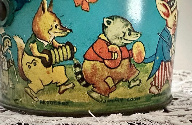 Puede incluir: Una fiambrera vintage de metal con una ilustraci&oacute;n colorida de cuatro animales de dibujos animados tocando m&uacute;sica. Los animales son un zorro tocando la tuba, un mapache tocando el pandero, un conejo tocando el tambor y un oso tocando la trompeta. El texto "Reddy Fox", "Jimmy Coon" y "Peter Rabbit" es visible en la fiambrera.