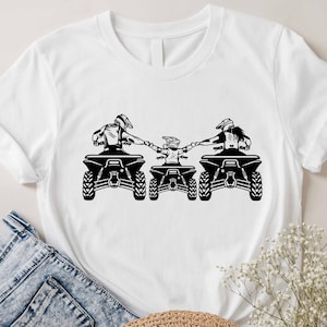 May include: A white t-shirt with a black silhouette of three people riding ATVs. The people are holding hands and the ATVs are facing forward.