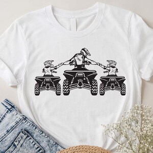 K&ouml;nnte beinhalten: Wei&szlig;es T-Shirt mit einer schwarzen Grafik von drei Personen, die auf Quads fahren. Die Personen halten sich an den H&auml;nden und die Quads sind nach vorne gerichtet.