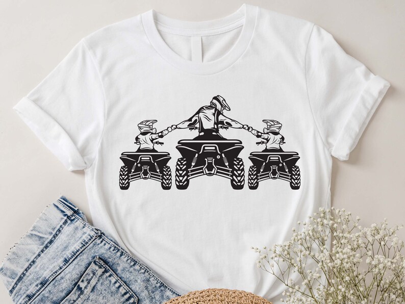 K&ouml;nnte beinhalten: Wei&szlig;es T-Shirt mit einer schwarzen Grafik von drei Personen, die auf Quads fahren. Die Personen halten sich an den H&auml;nden und die Quads sind nach vorne gerichtet.