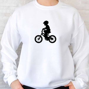 May include: White sweatshirt with a black silhouette of a child riding a bicycle.
