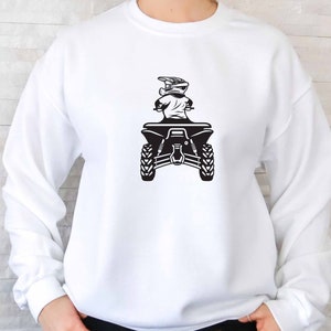 Puede incluir: Sudadera blanca con un gr&aacute;fico negro de una persona conduciendo un ATV. El ATV est&aacute; de espaldas al espectador y la persona lleva un casco.