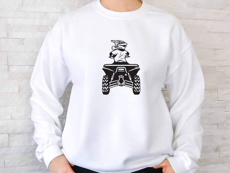 Puede incluir: Sudadera blanca con un gr&aacute;fico negro de una persona conduciendo un ATV. El ATV est&aacute; de espaldas al espectador y la persona lleva un casco.