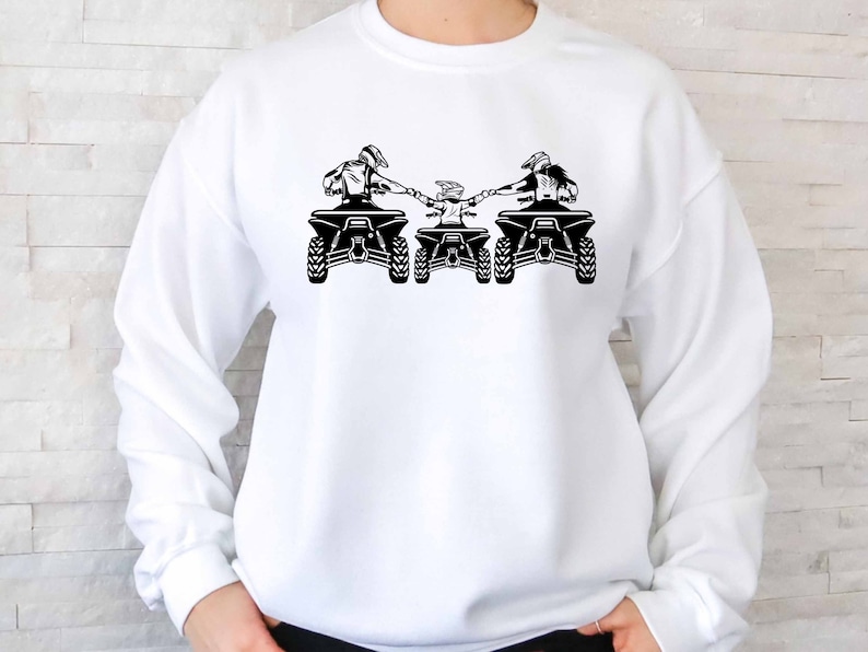 May include: White sweatshirt with a black graphic of three people riding ATVs. The people are holding hands and the ATVs are side by side.