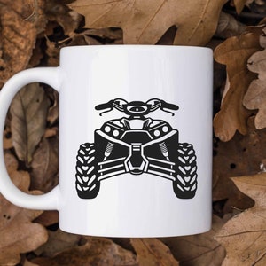 May include: White ceramic mug with a black silhouette of an ATV. The ATV has four wheels, a handlebar, and a seat.