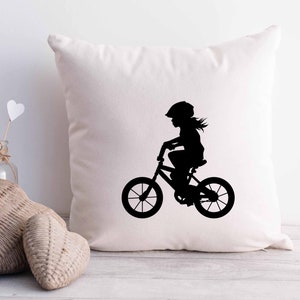 May include: White throw pillow with a black silhouette of a child riding a bicycle. The child is wearing a helmet.