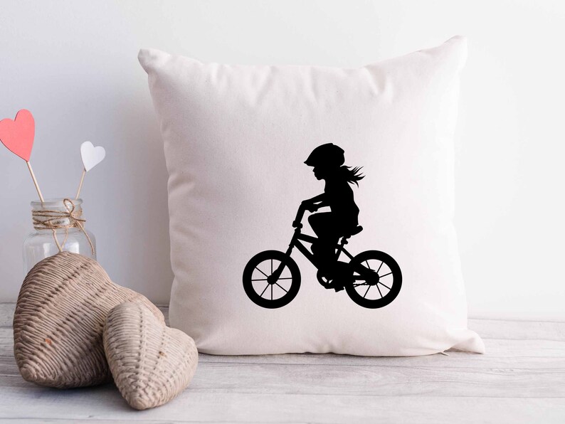 May include: White throw pillow with a black silhouette of a child riding a bicycle. The child is wearing a helmet.