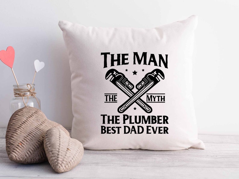 May include: White pillow with black text that reads "The Man The Myth The Plumber Best Dad Ever" with a graphic of two crossed wrenches.
