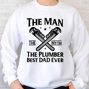 May include: White sweatshirt with black text that reads "The Man The Myth The Plumber Best Dad Ever". Two crossed wrench symbols are above the text.