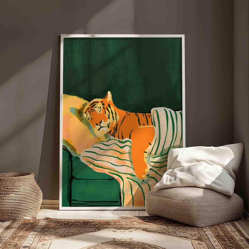 May include: A framed art print depicts an orange tiger resting on a green sofa with striped blankets and pillows. The tiger is the focal point, set against a dark green background. The artwork is in a white frame.