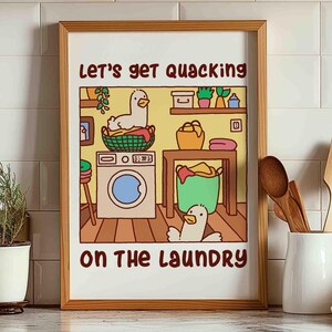 A colorful poster print of two ducks, or goose, doing the laundry. One is sitting in the dirty clothes basket and the other runs around.