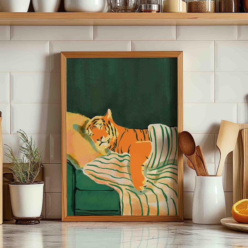 May include: A framed art print depicts an orange tiger resting on a green couch with striped bedding. The tiger is the focal point, with its stripes and relaxed pose. The artwork has a modern, illustrative style, with a green background.