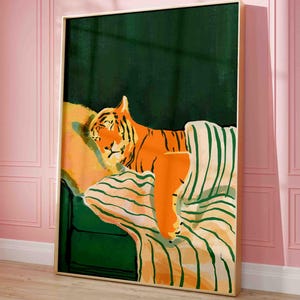 May include: A framed art print featuring an orange tiger resting on a green and striped sofa. The tiger has black stripes and is set against a dark green background. The artwork is in a gold frame and is displayed against a pink wall.