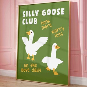 May include: A framed art print with a green background and the words "SILLY GOOSE CLUB" in white. Two cartoon geese are featured, along with the phrases "honk more", "worry less", and "on the loose daily". The frame is gold.
