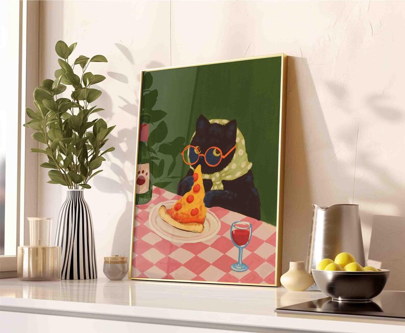 May include: A framed art print depicts a black cat wearing glasses and a scarf, enjoying a slice of pizza at a table with a checkered tablecloth. A bottle of wine and a glass of red wine are also on the table. The artwork has a gold frame.