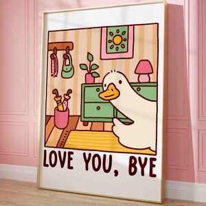 May include: A framed cartoon print featuring a large white duck with a yellow beak. The duck is in a room with a green dresser, a pink lamp, and the text "LOVE YOU, BYE". The background has a striped wallpaper.