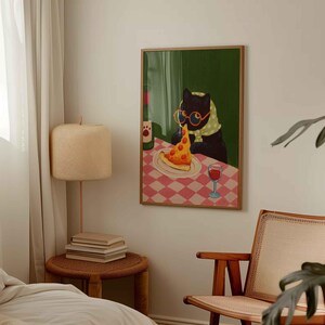 May include: A framed art print depicts a black cat wearing glasses and a scarf, enjoying a slice of pizza and a glass of wine. The cat sits at a table with a red and white checkered tablecloth. A bottle of wine is also on the table.