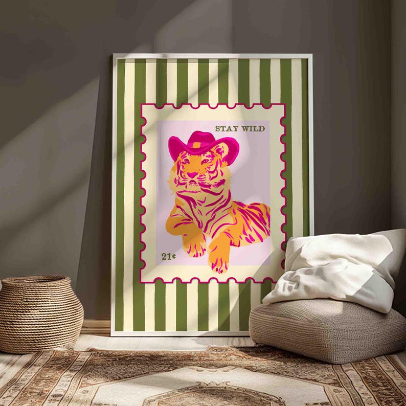 May include: A framed art print depicting a tiger in a pink cowboy hat, styled as a postage stamp. The tiger is orange and pink, with the text "STAY WILD" above and "21&cent;" below. The frame has a green and white striped design.